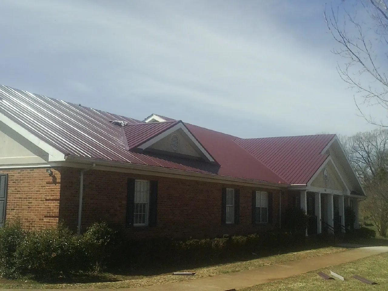 Red metal roof with gabled entries on a long brick building, from a Hail Damage Roof Repair job in Norfolk