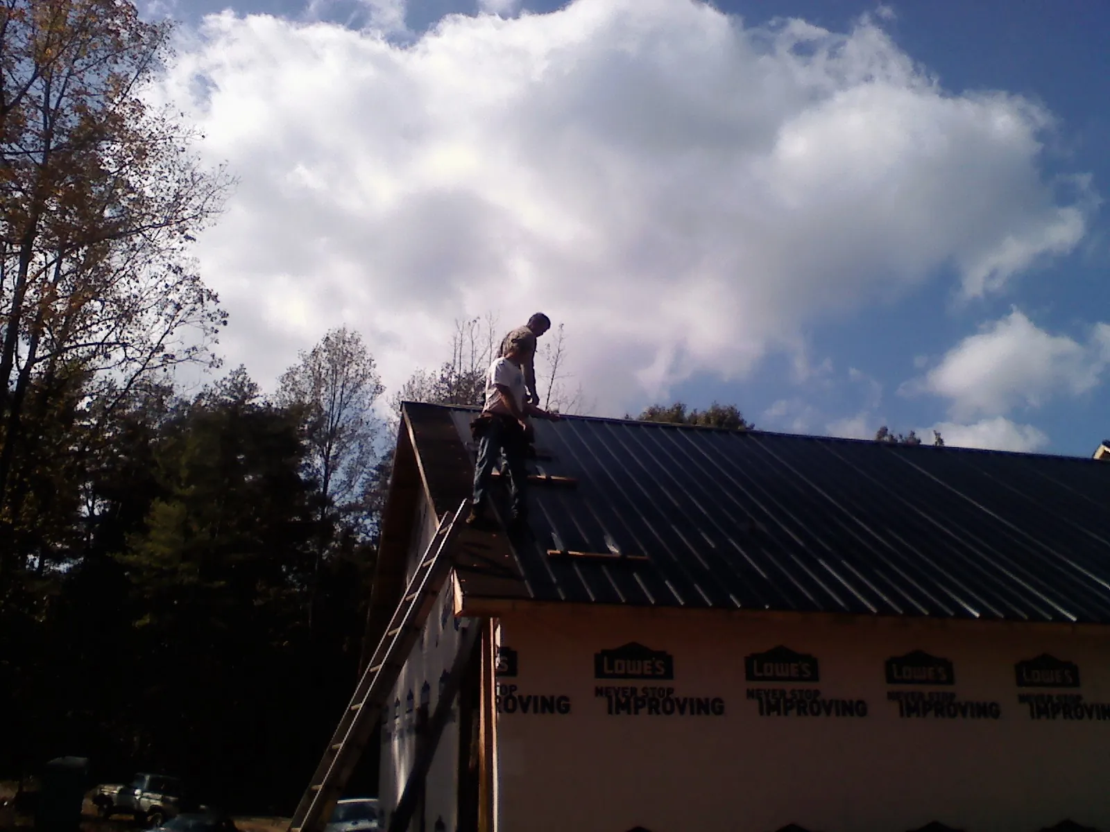 Roofer fastening dark metal panels high against a cloudy sky, from a Roof Inspection job in Norfolk