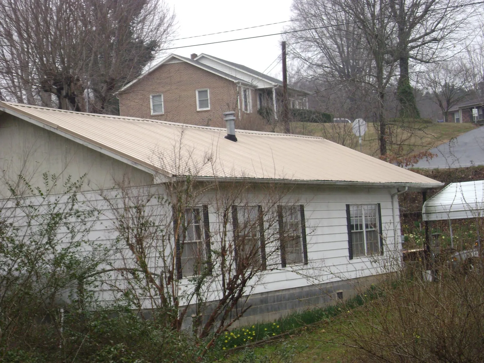 Tan metal roof on a white sided house set into a hillside — Commercial Roofing by Roofing Brothers in Norfolk