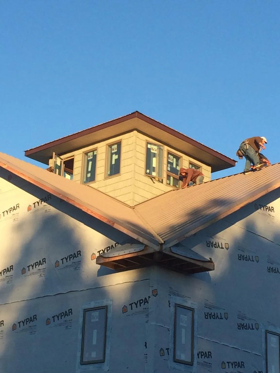 Roofers working around a rooftop cupola on a new metal roof at sunset — Roof Waterproofing in Norfolk by Roofing Brothers